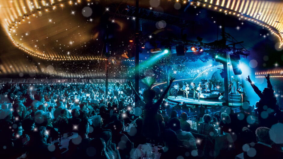 Stage with musicians and dancing audience under a tent decorated with lights at TIPI AM KANZLERAMT.
