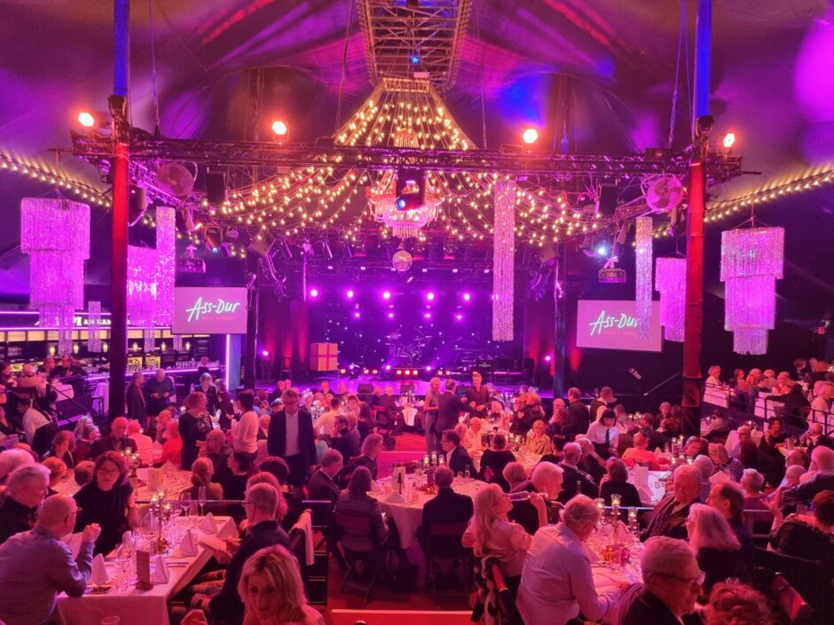 Große Veranstaltung in einem Zelt mit vielen Tischen, Gästen und lila Beleuchtung