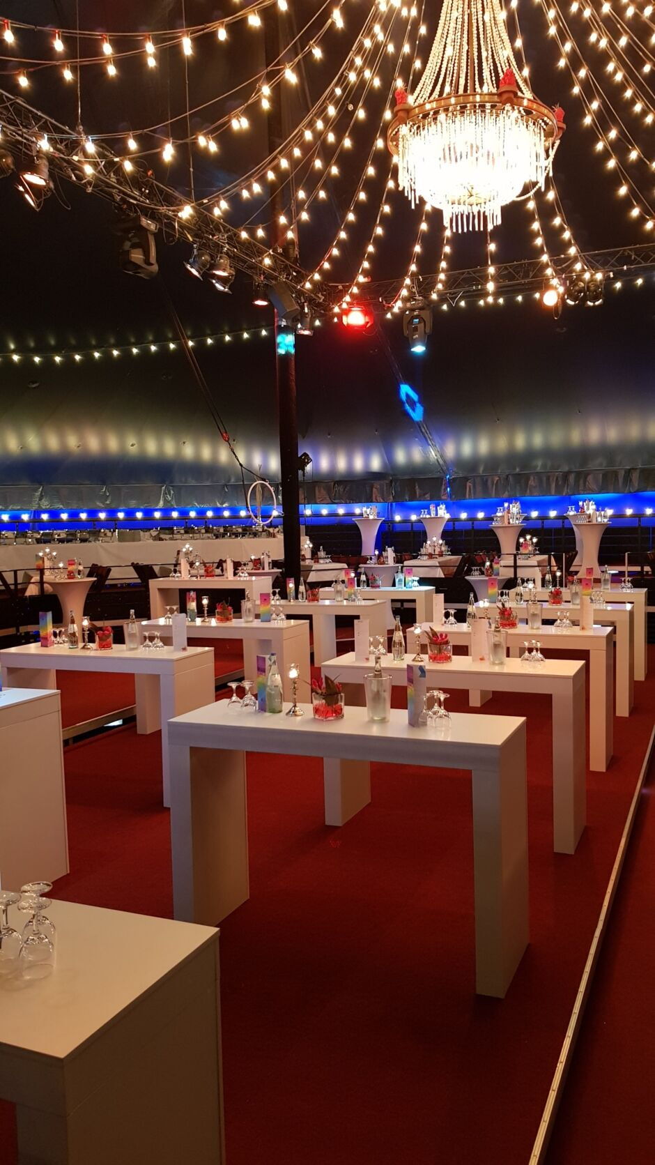 Festlich dekorierter Veranstaltungsraum mit weißen Tischen, Stühlen, Girlandenlichtern und einem großen Kronleuchter